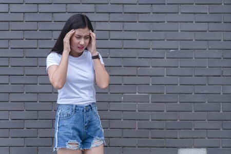 Stressd woman having migraine headache feeling pain.Sick asian female holding hands on head with bad feeling headache and stress. health and illness concept on gray background.の写真素材