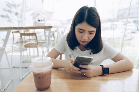 Young Asian woman using smartphone with smart watch on hand in coffee shop.
Japanese girl wearing smartwatch texting on mobile phone in  cafe, modern city technology lifestyle concept.の写真素材
