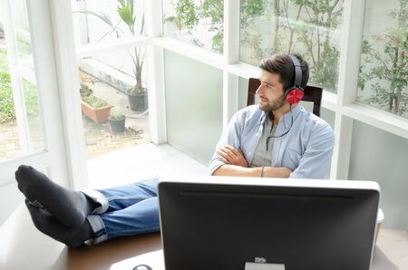 Men who work at home are relaxing by listening to music on the computer desk using headphones.