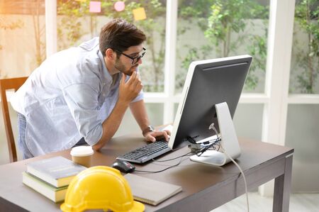 Engineers working within an office using a computer. He put the helmet on the sideの写真素材