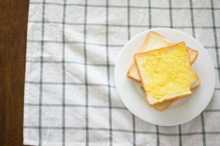 Buttered bread on a plate with a white table cloth pad below.の写真素材