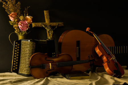 still life ,light and painting ,jesus cross violin quitar accordion on black background