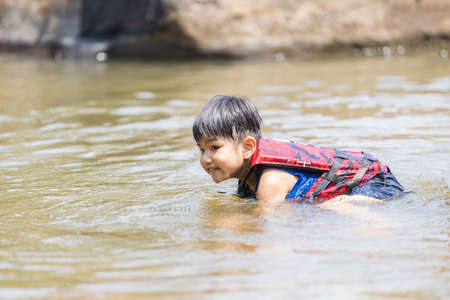 A little boy play water and water-fall , he is enjoy and happy ,swim and play ,He put on parachute for safetyの写真素材