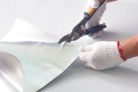 Worker hand with protective gloves holding a pair of scissors cutting a sheet of foilの写真素材