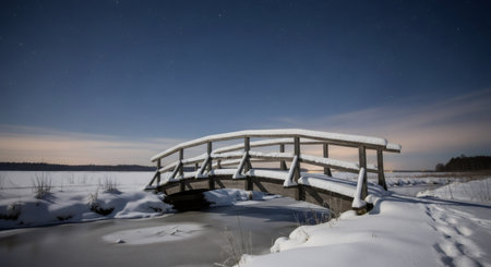 A snow-covered wooden bridge spans a partially frozen lake under a clear winter sky, creating a serene landscape.の素材