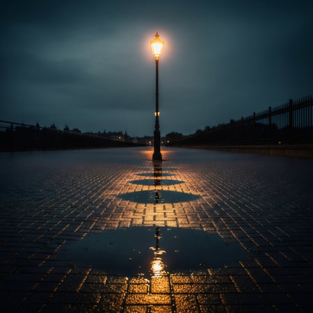 A solitary lamp post glows brightly, casting a warm light onto a wet brick pavement. The reflection creates a symmetrical pattern, enhancing the moody atmosphere of the night.の素材