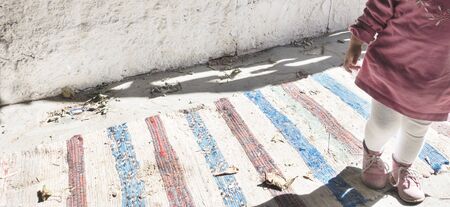Panorama view of little girl leg and small shoes standing on stripes rug with white wall behind.の写真素材