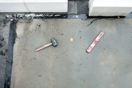 Top view on hammer and spirit level laying on the concrete, dirty floor with white wall under...