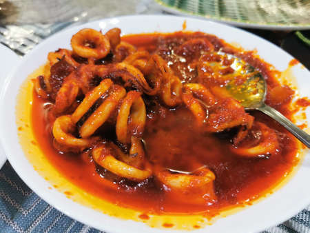 Spicy squid in sweet and sour sauce on white plate with spoonの写真素材