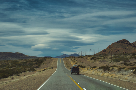 4x4 vehicle driving along a desert road on a cloudy day in a mountainous landscape in South Americaの写真素材