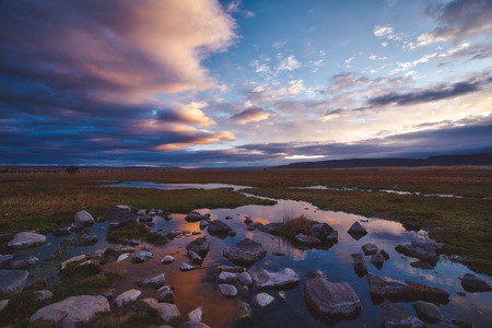 Pink sunset over wetlands in a scenic landscape with clouds reflected in the still water below and rocks in the foregroundの写真素材
