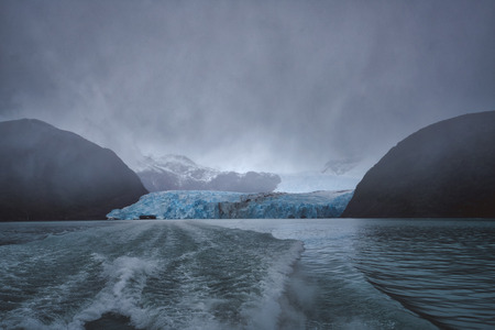 Wake of a tour boat leaving a large glacier between mountain peaks in Argentina in a moody overcast...