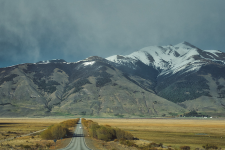 Receding tarred road in a mountainous landscape with snow covered peaks in Argentina, South Americaの写真素材