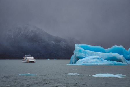 Tour boat looking at blue icebergs from a glacier in Argentina on a cold misty dayの写真素材