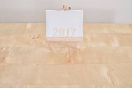 Alphabet 2017 on a three legged board made of cloth, standing on light brown table and white...