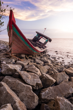 Long exposure image of abandoned wrecked wooden boat on rocky surface beside the ocean.の写真素材