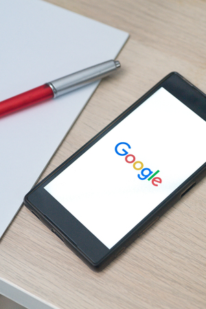 KUALA LUMPUR, MALAYSIA - OCTOBER 17, 2018: Google logo on smartphone on top of wooden table with book and pen. Google is changing the way it licenses its suite of Android apps.のeditorial素材