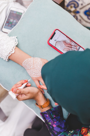 Closeup tight shot of focused young muslim woman painting henna on nervous bride hand. precise...