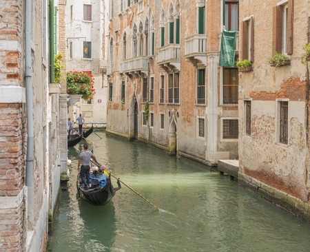 Venetian gondolier punting gondola through green canal waters of Italyのeditorial素材