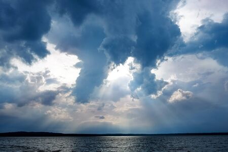 Storm clouds and sunbeams under lake before rain