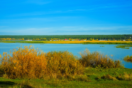River with bushes and cottages in early morning in autumnの写真素材