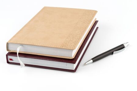 Two diary stacked lying next to a black pen on a white backgroundの写真素材