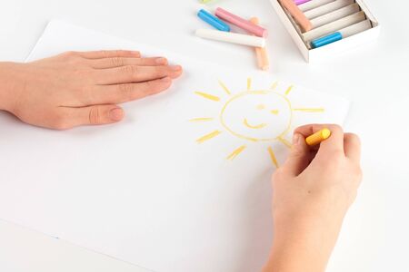 Child s hand drawing a pastel crayon smiling sunの写真素材