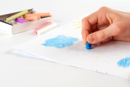 Child s hand, drawing a cloud of pastel crayon on white paper の写真素材