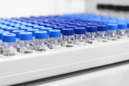 Rows of glass vials in the tray automatic liquid dispenser. Laboratory chemical equipments. Shallow...