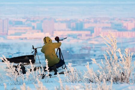 Man with photo camera on tripod taking timelapse photos winter panorama of the city.. Poor lighting conditions.の写真素材