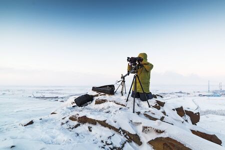 Man with photo camera on tripod taking timelapse photos in the arctic tundra. Poor lighting conditions.の写真素材