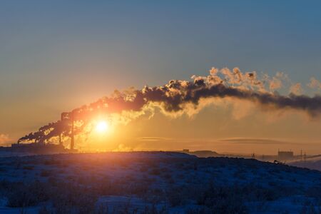 The setting sun makes its way through the dense smoke from the factory chimneys. Polar tundra, winter.の写真素材