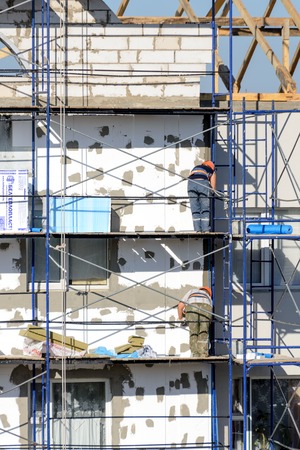 LYAKHOVICHI, BELARUS - AUGUST 28, 2016: Construction workers carry out work on plastering and insulation of external walls of the buildingのeditorial素材