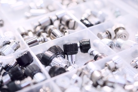 Many screws arranged as background. Metal fasteners, scattered in plastic cells.