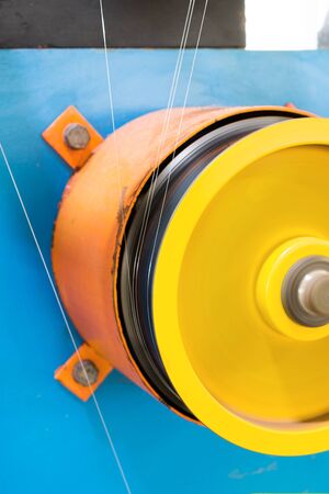 A rotating wheel rewinds a thin silver wire.