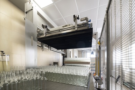 Automatic machine places empty glass bottles on a conveyor.