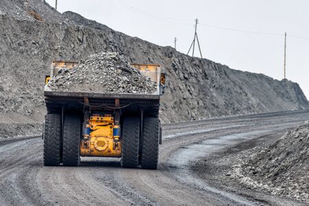 Quarry truck carries coal mined. A mining truck is driving along a mountain road. Road for the movement of heavy trucks.の写真素材
