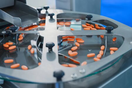 Pharmaceutical tablet manufacturing machine. Orange pills are sorted on a metal round conveyorの写真素材