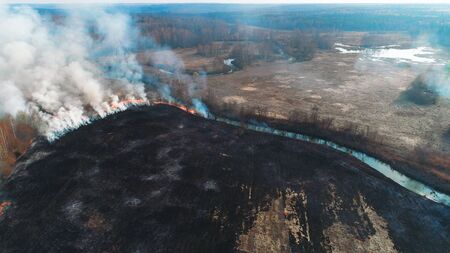 Forest and field fire. Dry grass burns, natural disaster. Aerial view. A large burned field, burning occurs on the banks of a small river.の写真素材