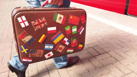 A man with a vintage suitcase comes into the vestibule of the train. The suitcase is decorated with stickers with the image of flags of different countries.の写真素材