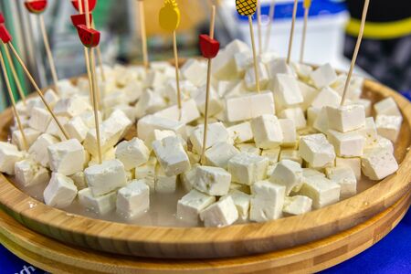 Diced fetax cheese. Pile in a wooden plate. Wooden toothpicks, tasting slices are stuck in pieces of cheese.の写真素材