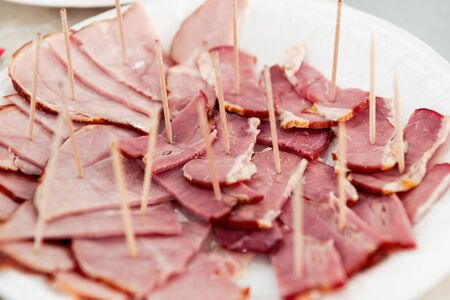 Thin slices of meat, ham, bacon lie on a white plate.の写真素材