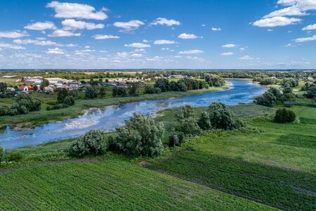 A small river flowing through meadows and agricultural fields. Aerial view. Evening shot with the setting sun.の写真素材