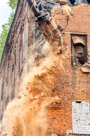 An excavator breaks a red brick wall. A lot of dust and falling debris and pieces.の写真素材