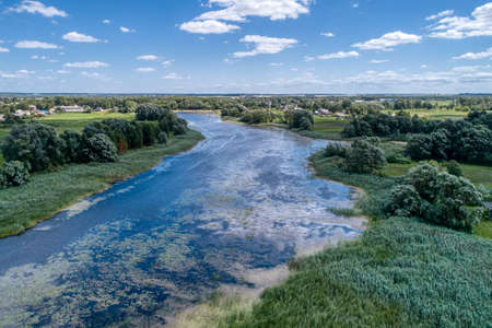 A small river flowing through meadows and agricultural fields. Aerial view. Evening shot with the...