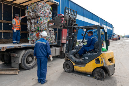 A forklift loads bales of compressed plastic bottles into a truck trailer. Transportation of triple plastic.のeditorial素材