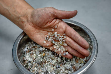 The hand pours the diamonds from the palm into a metal bowl. Many small gemsの写真素材