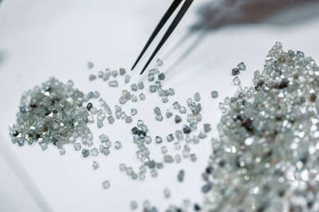 A hand holding tweezers transfers diamonds from one pile to another. Discarding precious stones on a white sheetの写真素材