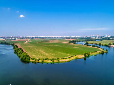 Large green field and trees near tranquil river in springの写真素材