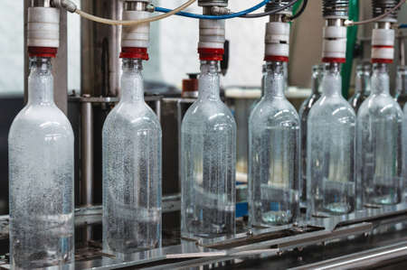 Equipment pours vodka into glass bottles on production line